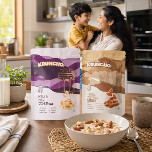 Kruncho Cashew and Almond pouches displayed on a wooden table beside a bowl of oatmeal with nuts, with a mother and child smiling in the background kitchen.