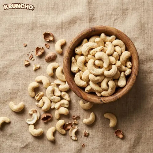 Whole cashew nuts in a wooden bowl on a linen tablecloth, with KRUNCHO branding.