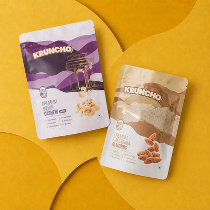 Two pouches of Kruncho dry fruits, featuring Premium Indian Cashews and Premium California Almonds, displayed on a textured yellow surface.