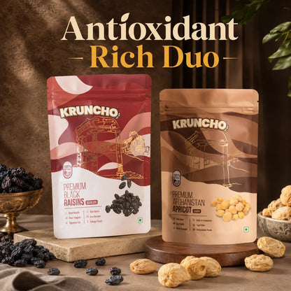 Packages of Kruncho Premium Black Raisins and Afghanistan Apricots sit on rustic wooden and stone risers, surrounded by loose raisins and dried apricots under the headline "Antioxidant Rich Duo".