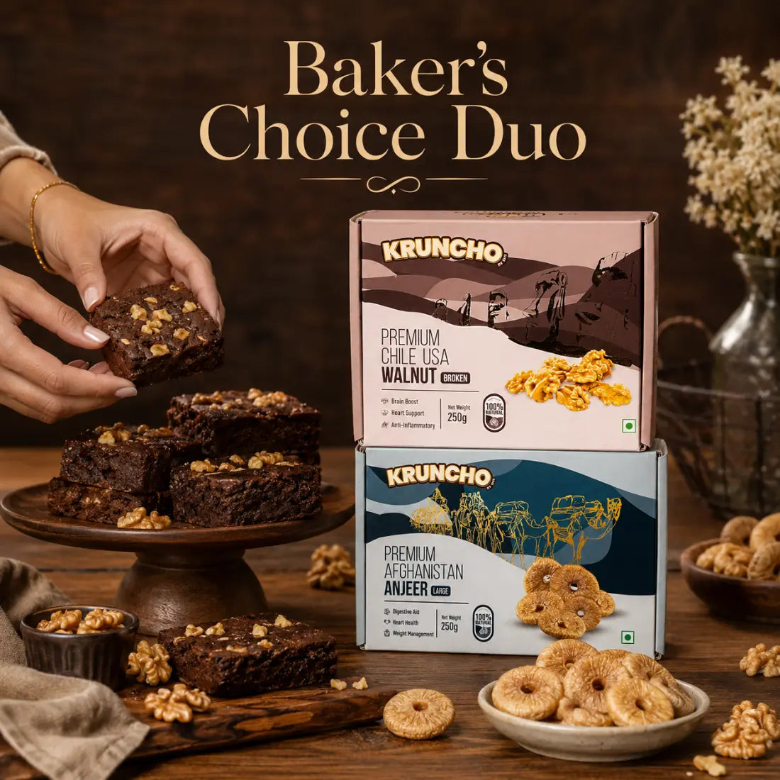 A pair of hands picks up a freshly baked walnut brownie from a wooden stand next to stacked boxes of KRUNCHO Premium Walnuts and Anjeer, under the text "Baker's Choice Duo."