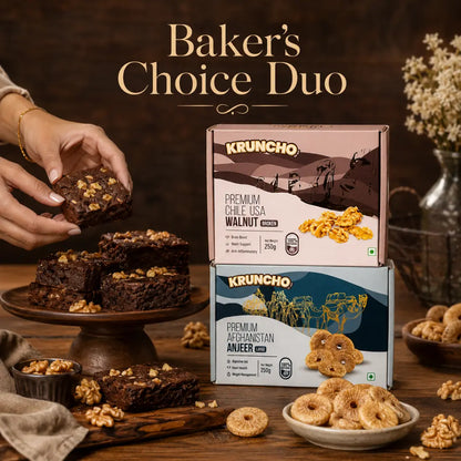 A pair of hands picks up a freshly baked walnut brownie from a wooden stand next to stacked boxes of KRUNCHO Premium Walnuts and Anjeer, under the text "Baker's Choice Duo."